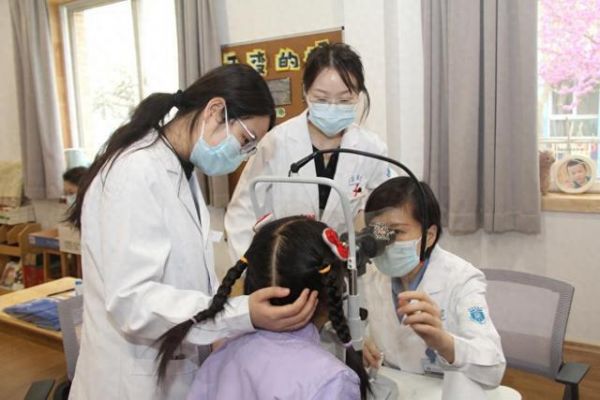 图为空军军医大学西京医院眼科主任医师窦国睿(右一)在幼儿园为小朋友进行眼部检查。新华社发